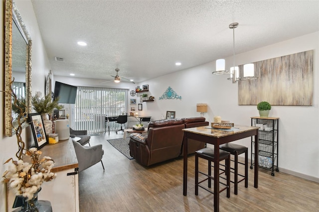 living room featuring ceiling fan with notable chandelier, a textured ceiling, and hardwood / wood-style flooring