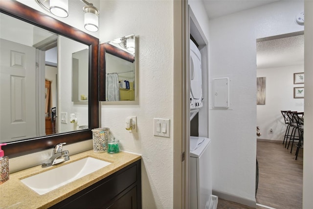 bathroom with vanity, wood-type flooring, stacked washing maching and dryer, and a textured ceiling