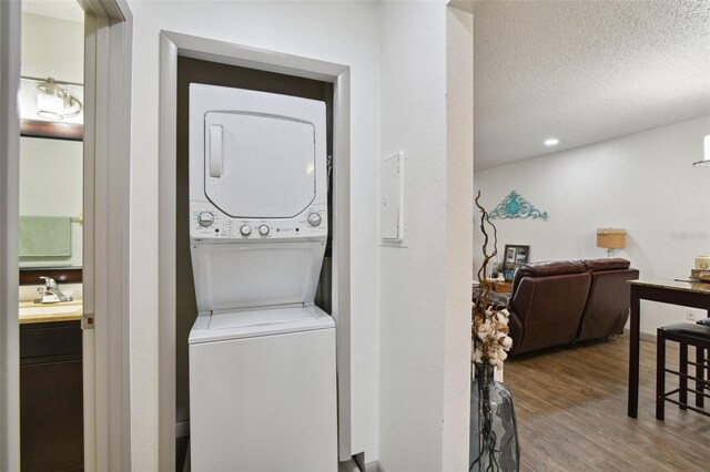 washroom with a textured ceiling, sink, wood-type flooring, and stacked washer and dryer