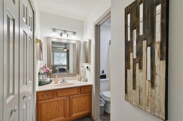 bathroom with vanity, a textured ceiling, toilet, and ceiling fan