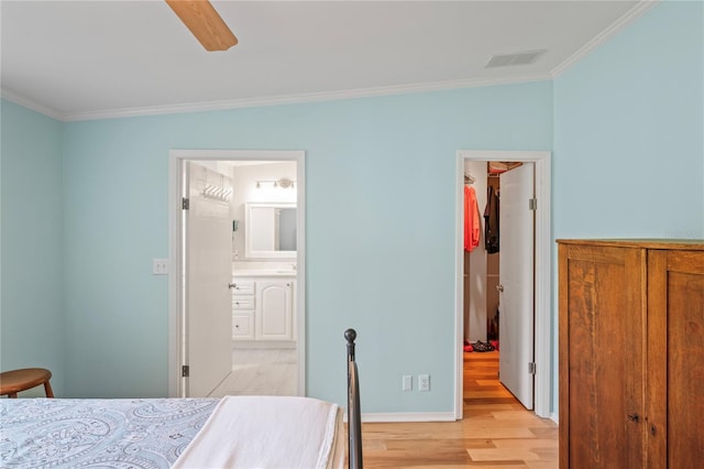 bedroom with ensuite bathroom, a walk in closet, ornamental molding, and light hardwood / wood-style flooring