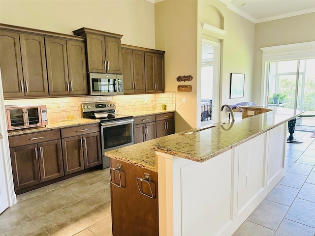 kitchen featuring light stone countertops, sink, crown molding, a kitchen island with sink, and appliances with stainless steel finishes