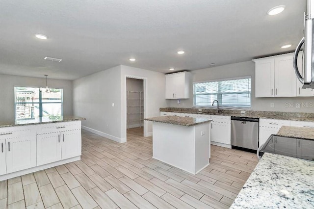 kitchen featuring dishwasher, a center island, light stone counters, and white cabinetry