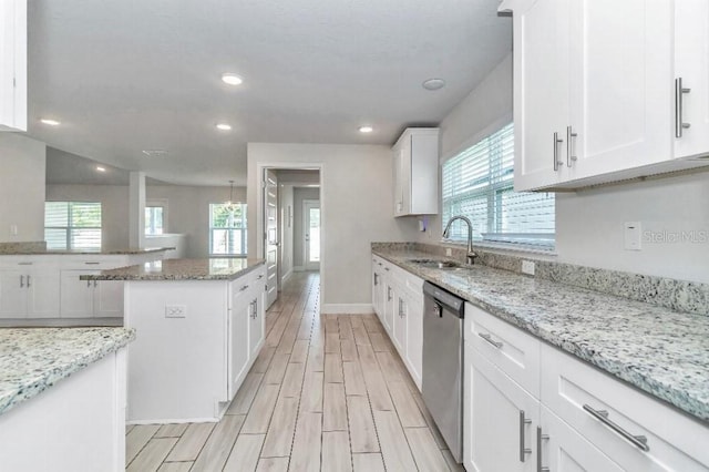 kitchen with white cabinets, sink, stainless steel dishwasher, light stone countertops, and a healthy amount of sunlight