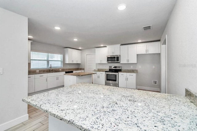 kitchen featuring appliances with stainless steel finishes, light stone counters, a kitchen island, sink, and white cabinetry