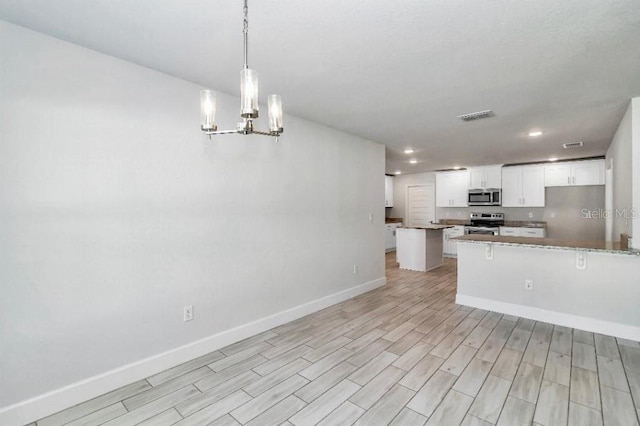 kitchen with kitchen peninsula, light stone counters, stainless steel appliances, decorative light fixtures, and white cabinetry