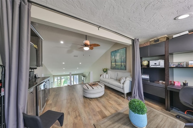 living room with a textured ceiling, vaulted ceiling, ceiling fan, and light wood-type flooring