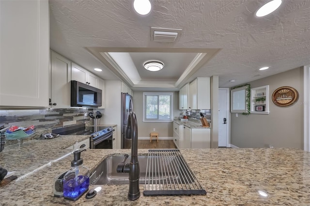 kitchen with appliances with stainless steel finishes, a raised ceiling, light stone countertops, decorative backsplash, and white cabinets