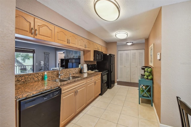 kitchen with black appliances, dark stone countertops, light tile patterned floors, and sink