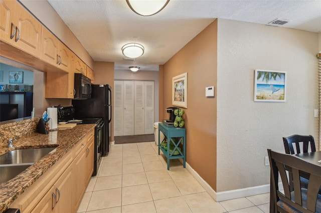 kitchen featuring sink, black appliances, light brown cabinets, light tile patterned floors, and dark stone countertops