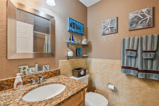 bathroom with walk in shower, vanity, tile walls, and toilet