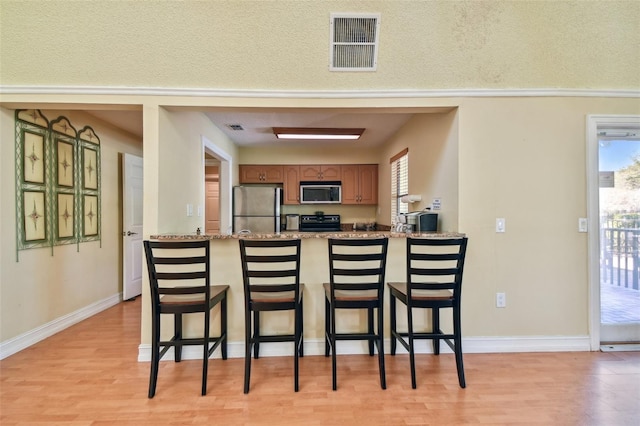 kitchen with a breakfast bar, stainless steel appliances, light stone counters, and a healthy amount of sunlight