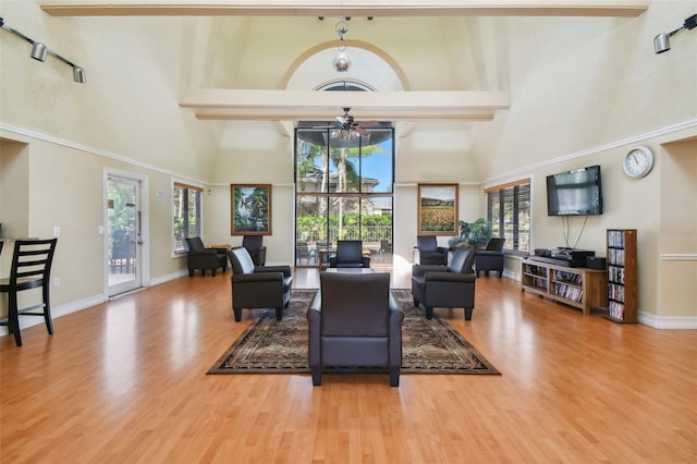 living room with ceiling fan, plenty of natural light, a towering ceiling, and hardwood / wood-style flooring