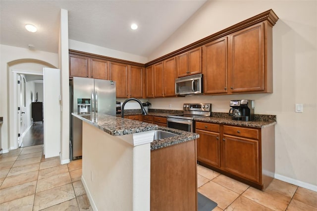 kitchen featuring stainless steel appliances, sink, dark stone countertops, lofted ceiling, and an island with sink