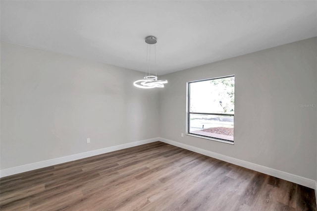 empty room with wood-type flooring and a chandelier