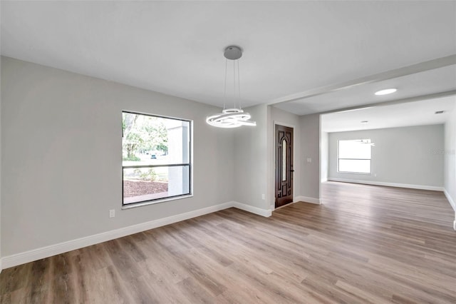 spare room featuring an inviting chandelier, plenty of natural light, and light hardwood / wood-style floors