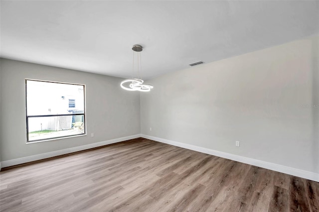 spare room featuring an inviting chandelier and light hardwood / wood-style flooring