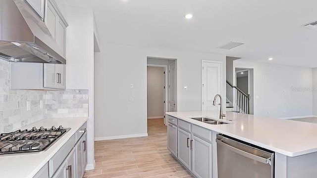 kitchen with sink, gray cabinets, an island with sink, tasteful backsplash, and stainless steel appliances