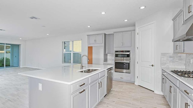 kitchen featuring stainless steel appliances, a center island with sink, tasteful backsplash, and sink