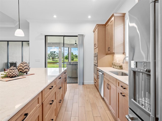 kitchen featuring stainless steel appliances, a sink, light stone countertops, decorative light fixtures, and crown molding