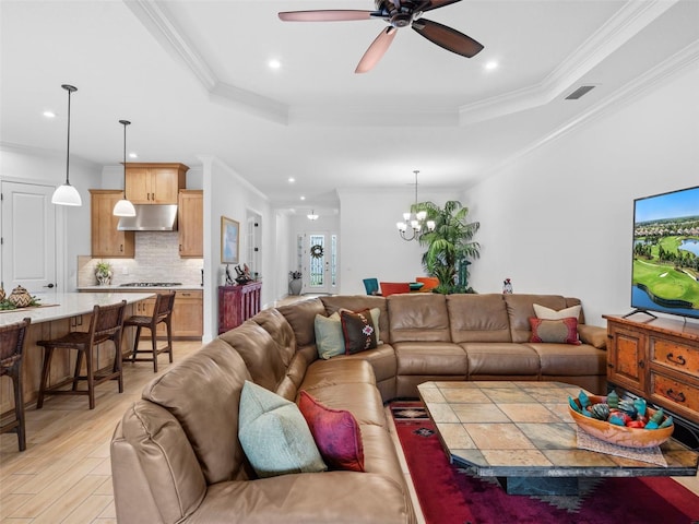 living room with visible vents, a raised ceiling, ornamental molding, light wood-type flooring, and ceiling fan with notable chandelier