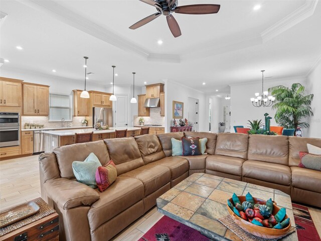 living room featuring a tray ceiling, crown molding, recessed lighting, light wood-style floors, and ceiling fan with notable chandelier