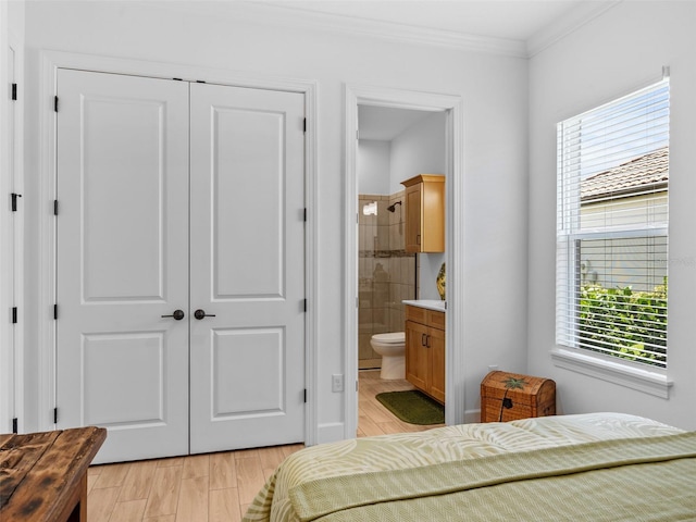 bedroom featuring ornamental molding, light wood-type flooring, a closet, and ensuite bath