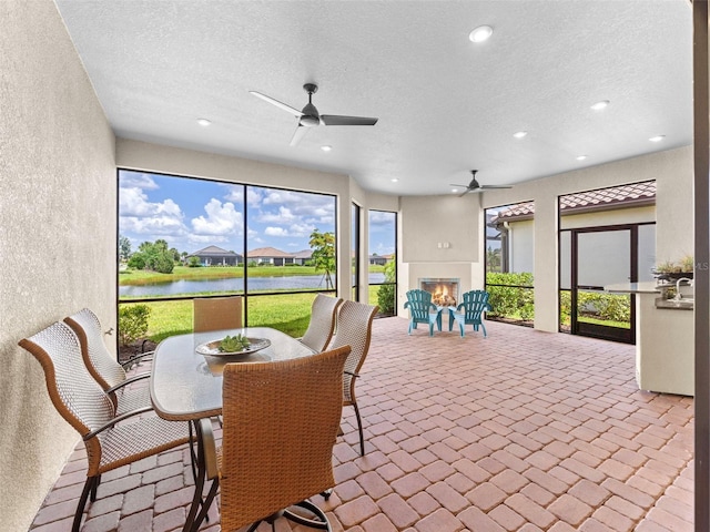 sunroom with ceiling fan and a water view