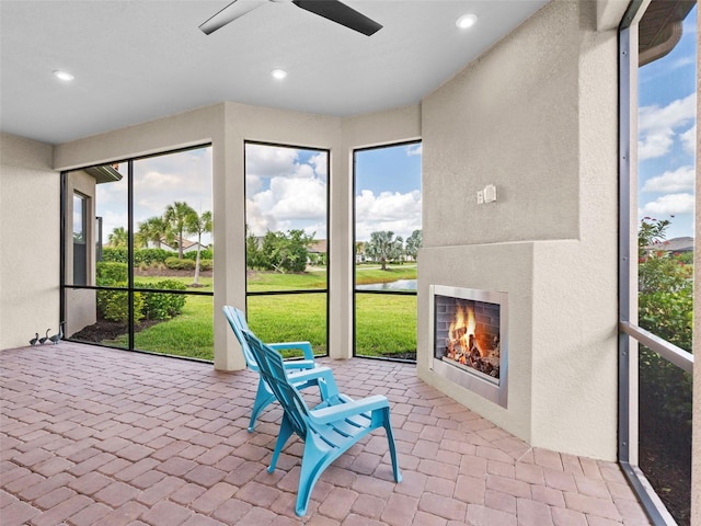 sunroom with a warm lit fireplace and a ceiling fan