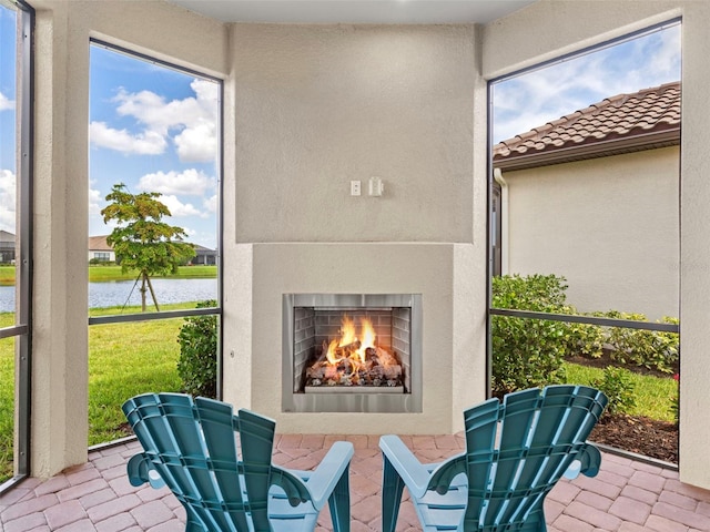 view of patio with a warm lit fireplace and a water view