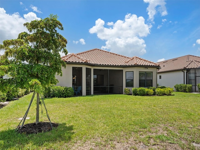 rear view of house with a sunroom, a tile roof, a lawn, and stucco siding