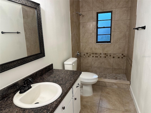 bathroom with toilet, tile patterned flooring, tiled shower, and vanity