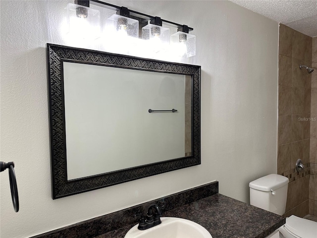 bathroom featuring a textured ceiling, toilet, tiled shower, and vanity