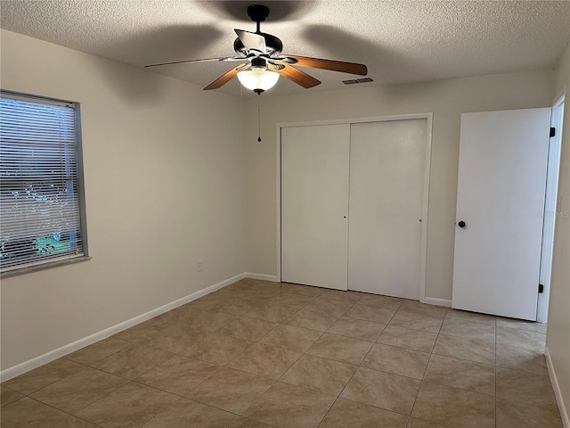 unfurnished bedroom with a textured ceiling, ceiling fan, light tile patterned floors, and a closet