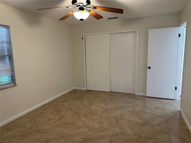 unfurnished bedroom with ceiling fan, light tile patterned floors, a closet, and a textured ceiling