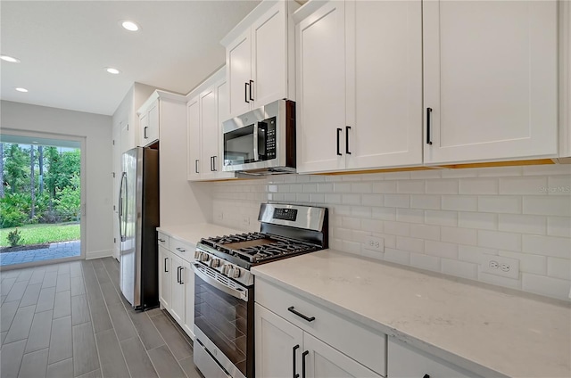 kitchen with light hardwood / wood-style flooring, appliances with stainless steel finishes, tasteful backsplash, light stone counters, and white cabinetry