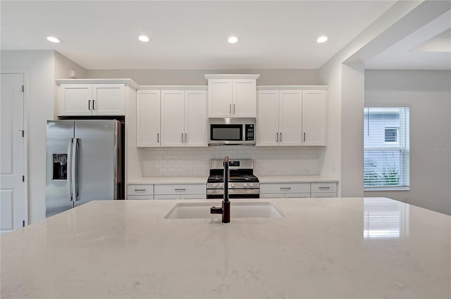 kitchen featuring backsplash, light stone countertops, white cabinets, and stainless steel appliances