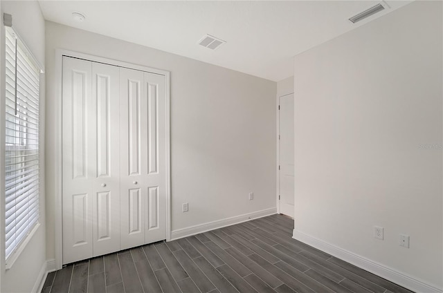 unfurnished bedroom with multiple windows, a closet, and dark wood-type flooring