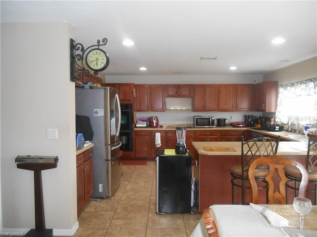 kitchen with a center island, range hood, light tile floors, and appliances with stainless steel finishes