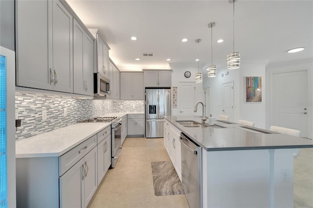 kitchen with sink, hanging light fixtures, backsplash, a kitchen island with sink, and appliances with stainless steel finishes