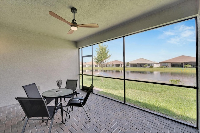 sunroom with ceiling fan and a water view