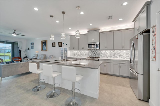 kitchen with ceiling fan, hanging light fixtures, stainless steel appliances, a breakfast bar, and a center island with sink