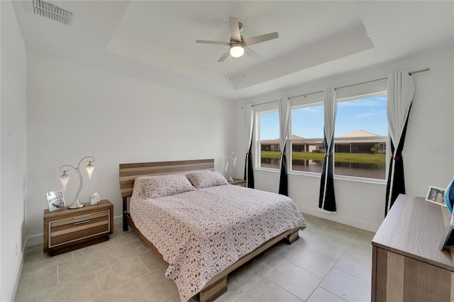 bedroom featuring ceiling fan, a water view, light tile patterned floors, and a tray ceiling