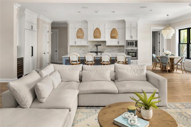 living room featuring light wood-type flooring, crown molding, a notable chandelier, and beverage cooler