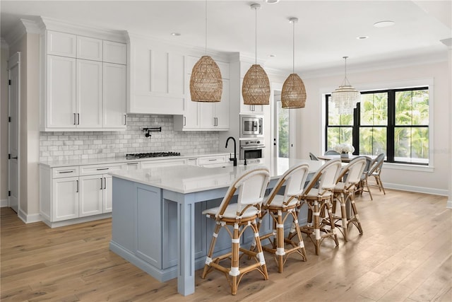 kitchen featuring appliances with stainless steel finishes, white cabinetry, sink, decorative light fixtures, and an island with sink