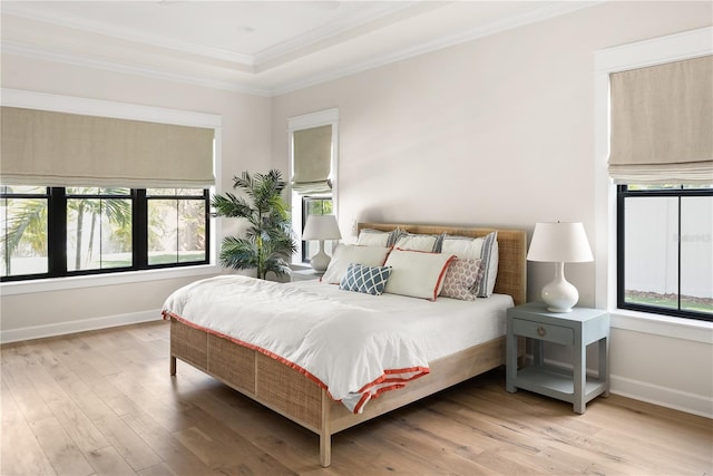 bedroom with a tray ceiling, crown molding, and light wood-type flooring