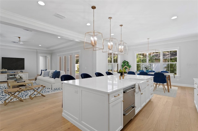 kitchen with white cabinets, hanging light fixtures, a kitchen island with sink, and a healthy amount of sunlight