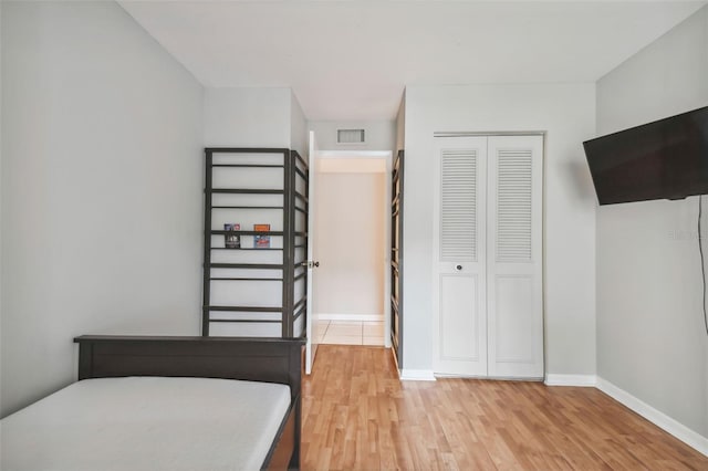 bedroom with light wood-style floors, baseboards, visible vents, and a closet