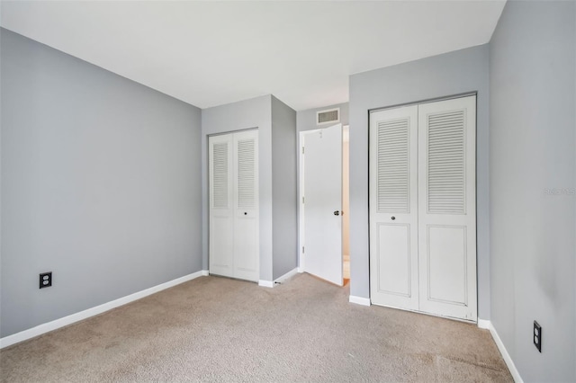 unfurnished bedroom featuring carpet floors, two closets, visible vents, and baseboards