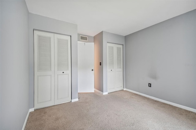 unfurnished bedroom featuring carpet floors, baseboards, visible vents, and multiple closets